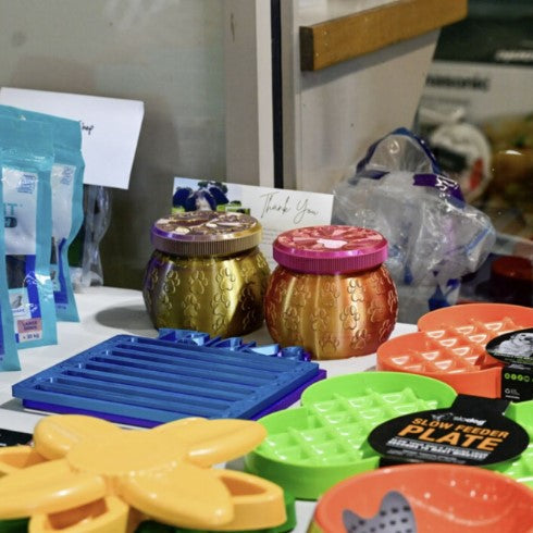 Assorted colorful pet toys and feeders on a table with a kitchen background.