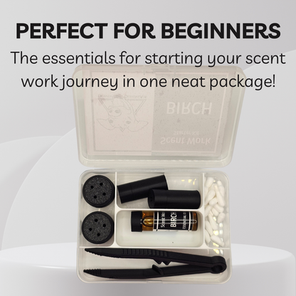 A beginner's scent work kit in a clear plastic case, shown open on a light gray background with promotional text at the top. The kit includes black vessels, a small amber bottle labeled BIBCH, white cotton tips, black tweezers, and black magnetic vessels.