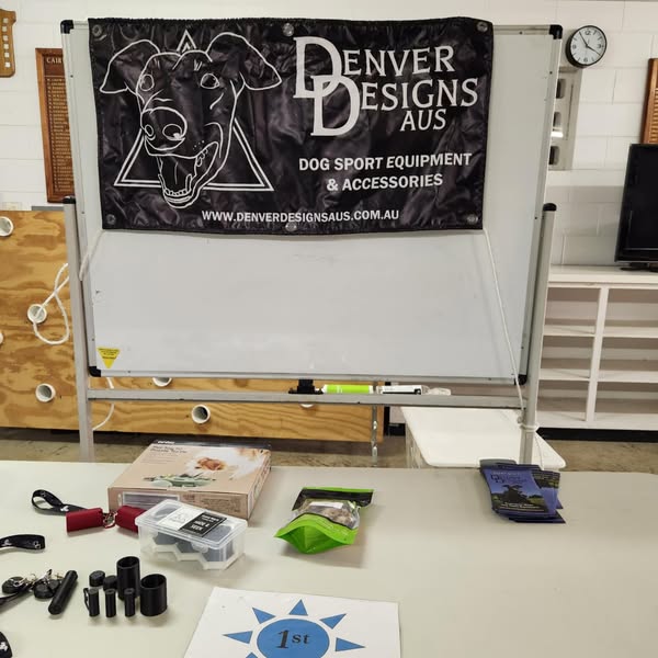 Denver Designs Aus banner on a whiteboard with dog sport equipment and accessories on a table.