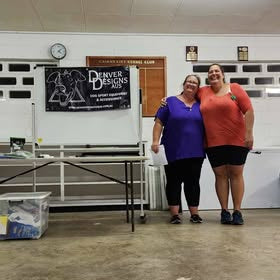 Two women standing in a room with a table and posters on the wall.