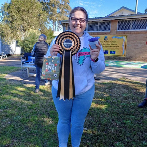 Person holding a ribbon and a small object outdoors with a building and trees in the background