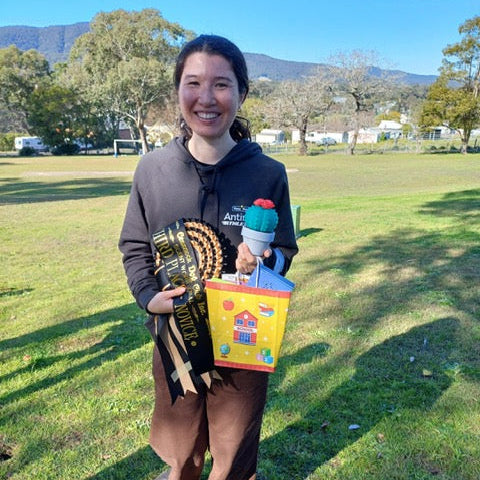 Person holding prizes in a park with trees and mountains in the background