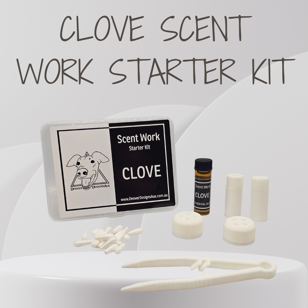 Clove Scent Work Starter Kit containing a small plastic case with a black and white label, a small amber bottle, white magnetic vessels, white cylindrical brick wall vessels, and white tweezers, arranged on a white surface with a gray background and the text 'CLOVE SCENT WORK STARTER KIT' at the top.