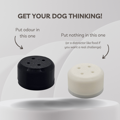 Two cylindrical dog training magnetic scent vessel shown on a light gray graphic background with explanatory text. The left device is black and labeled 'Put odour in this one,' and the right device is white and labeled 'Put nothing in this one (or a distractor like food if you want a real challenge).