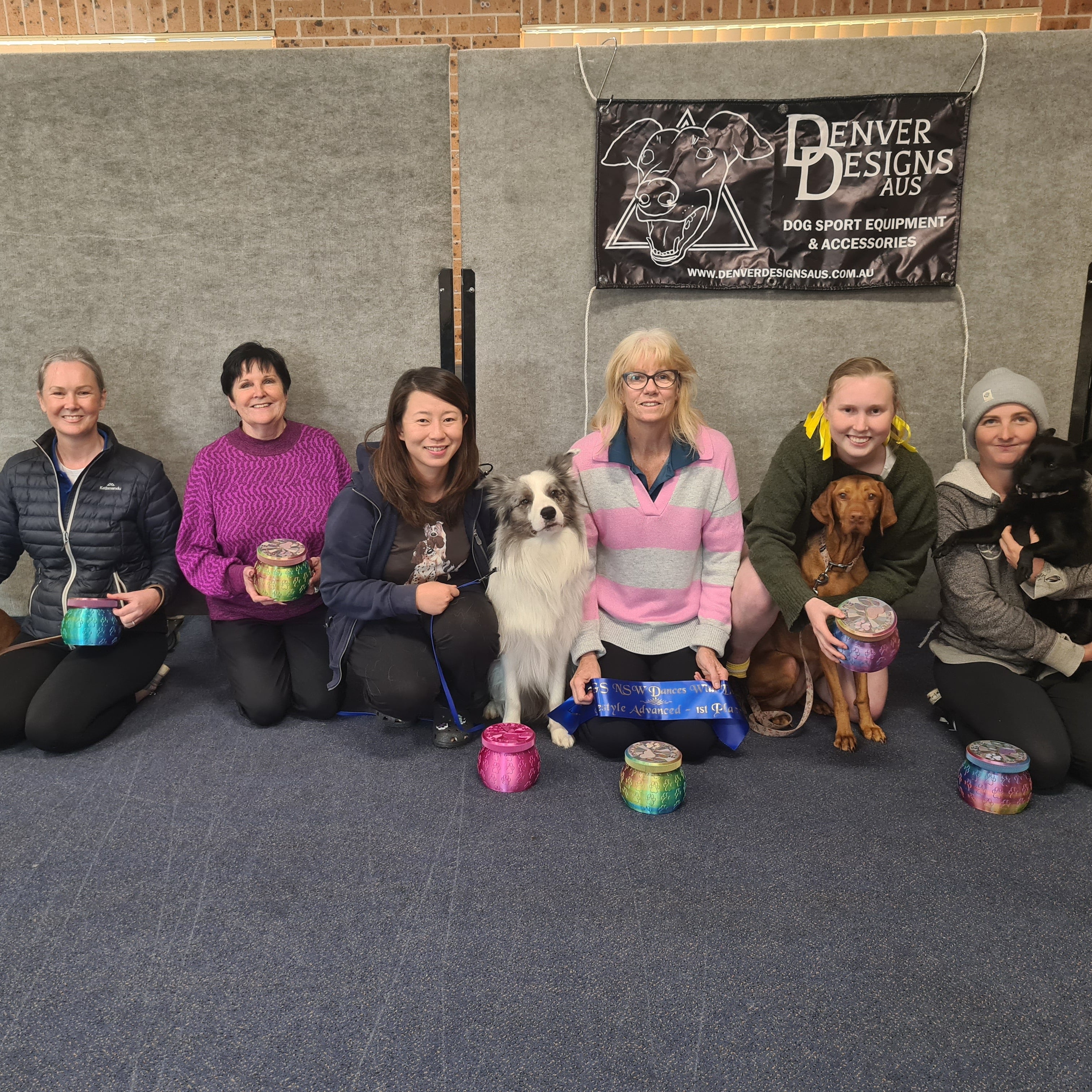 Group of people with dogs in a room with a 'Denver Designs' banner.