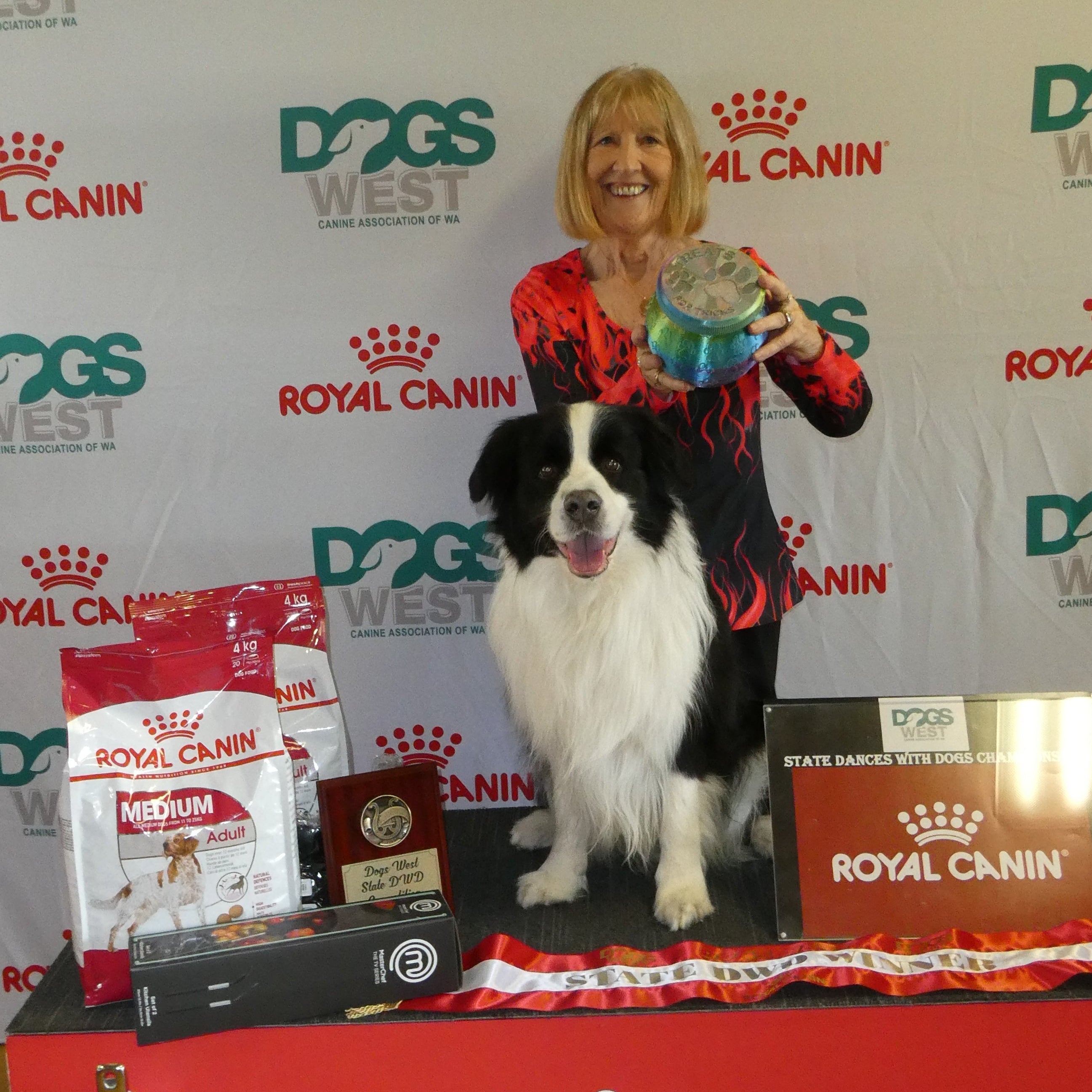 Woman with a dog holding a trophy in front of a Royal Canin and Dogs West backdrop