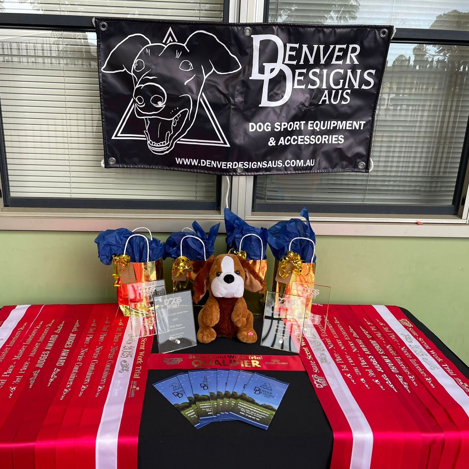 Table with dog-themed products and a Denver Designs Aus banner in the background.