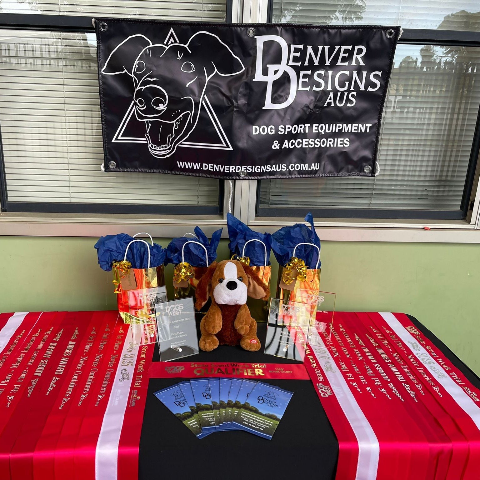 Table with dog-themed products and a Denver Designs Aus banner in the background.
