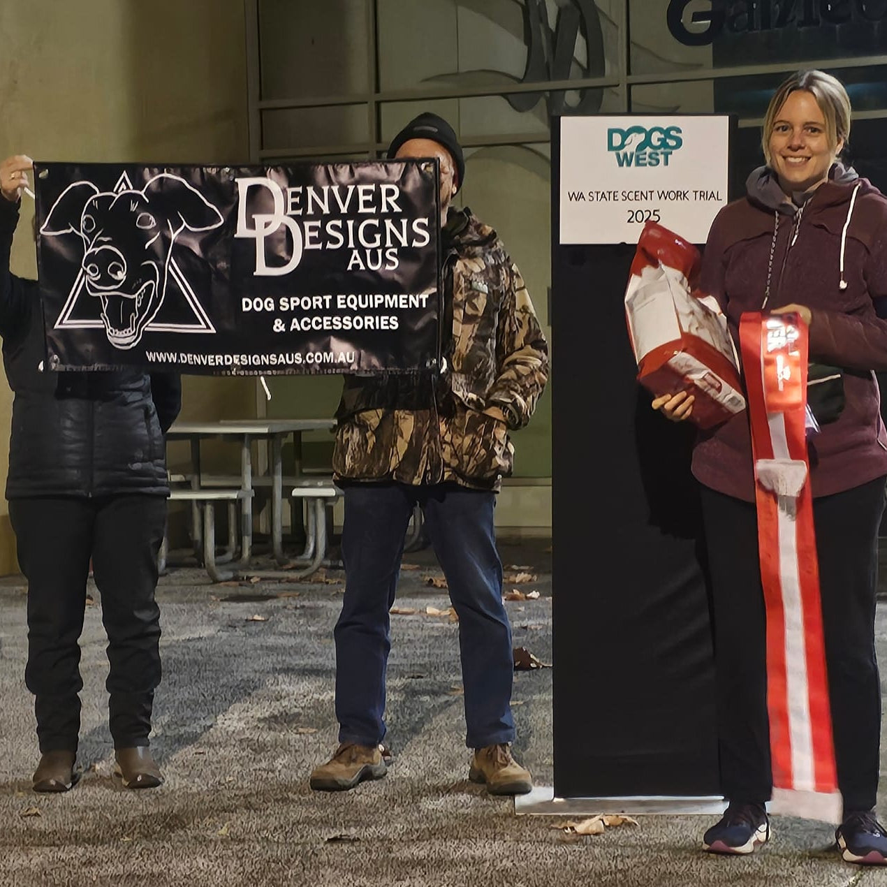Three people holding signs and a dog toy in an outdoor setting.