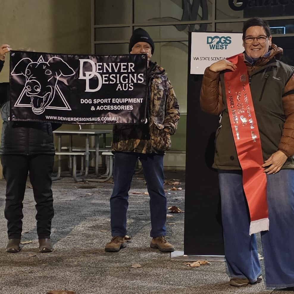Two people holding signs for Denver Designs and Dog West, with one person wearing a sash.