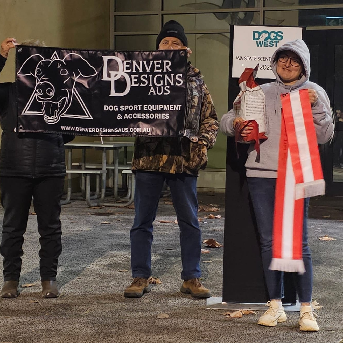Three people holding signs and a dog in an outdoor setting