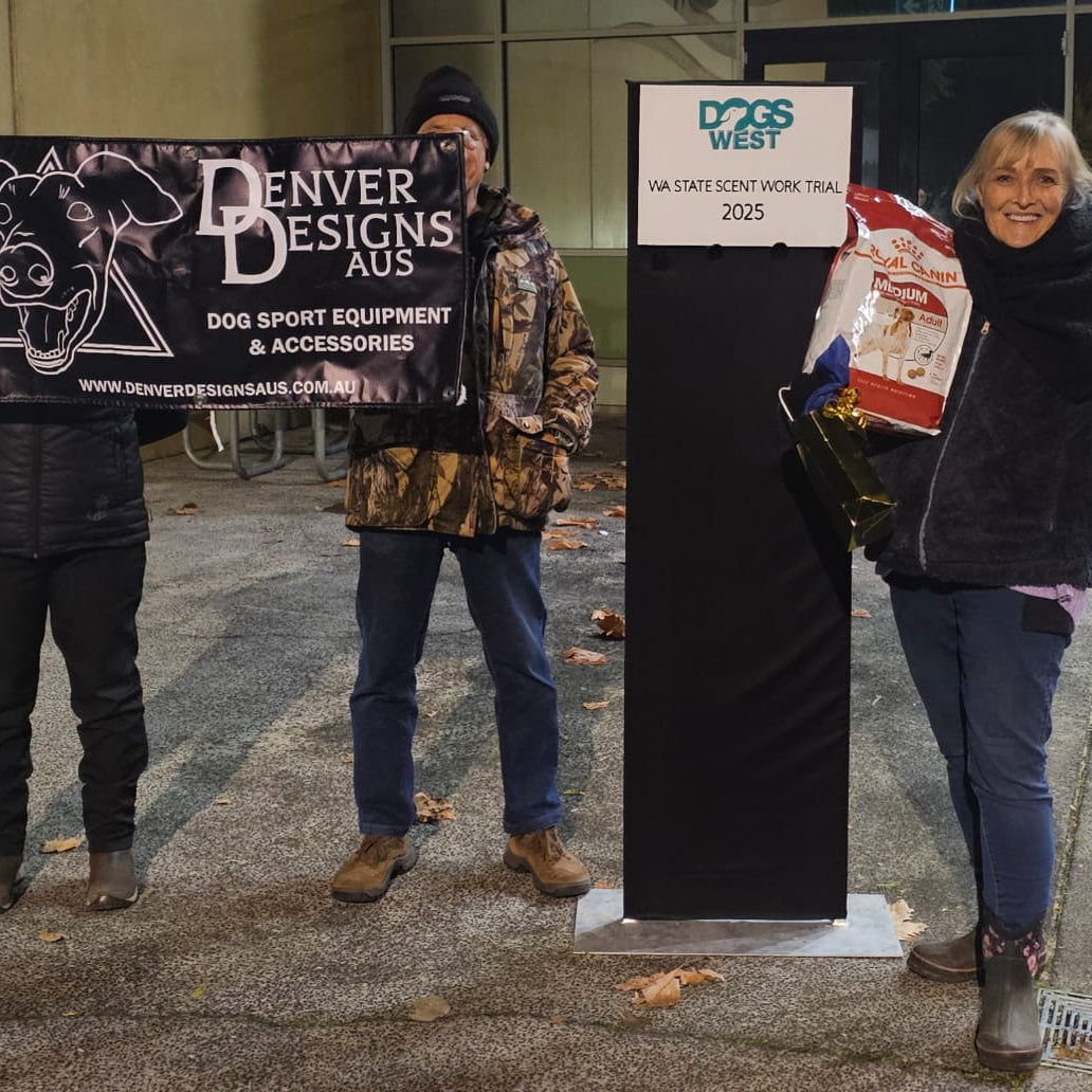 Three people holding signs and a stand with a product display, outdoors.