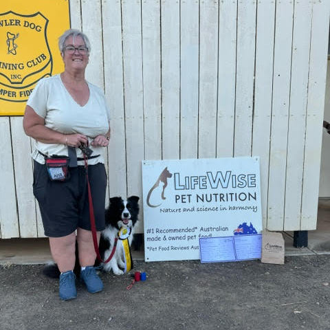 Woman with a dog standing next to a LifeWise Pet Nutrition sign.