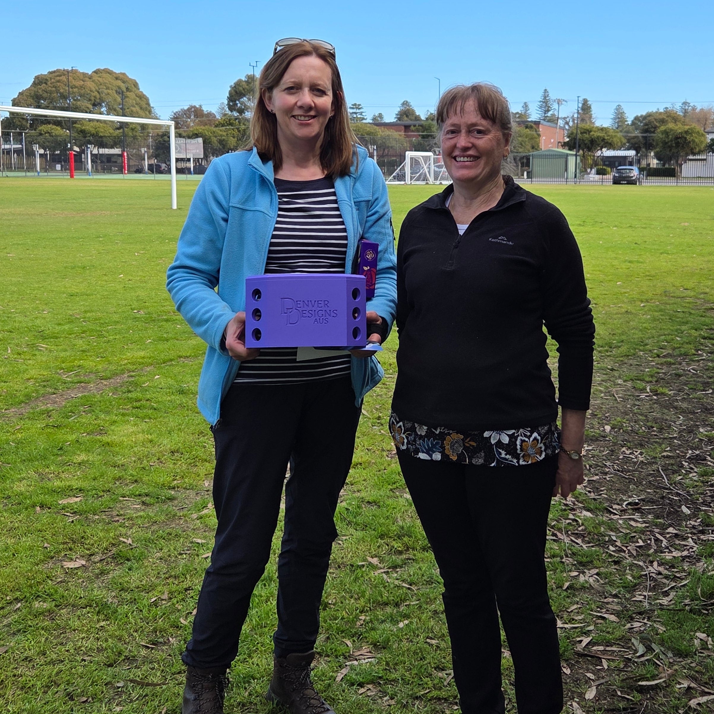 Two people standing on a grassy field with a clear blue sky.