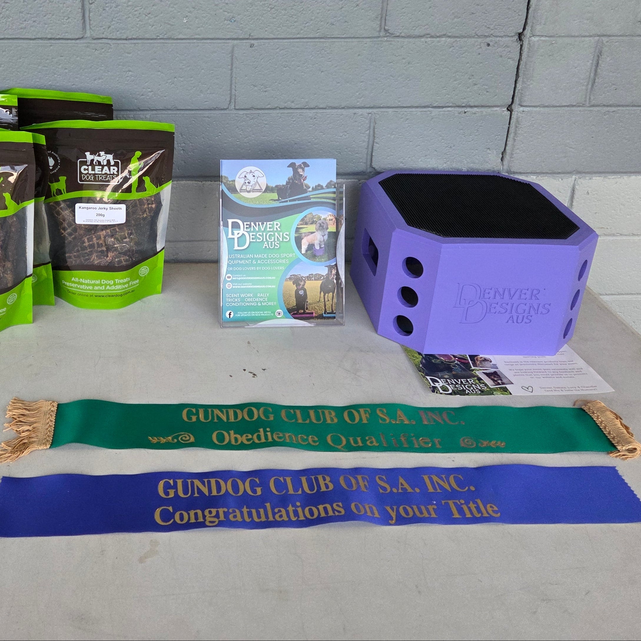 Collection of dog food packages, a purple container, and a banner on a concrete surface with a gray brick wall background.