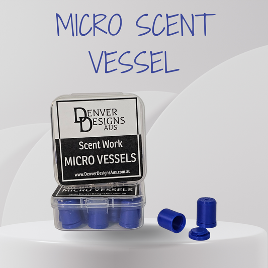 A clear plastic case containing several small blue cylindrical micro scent vessels, with two loose blue vessels placed beside it on a white surface. The front label reads 'Denver Designs Aus' and 'Scent Work Micro Vessels.