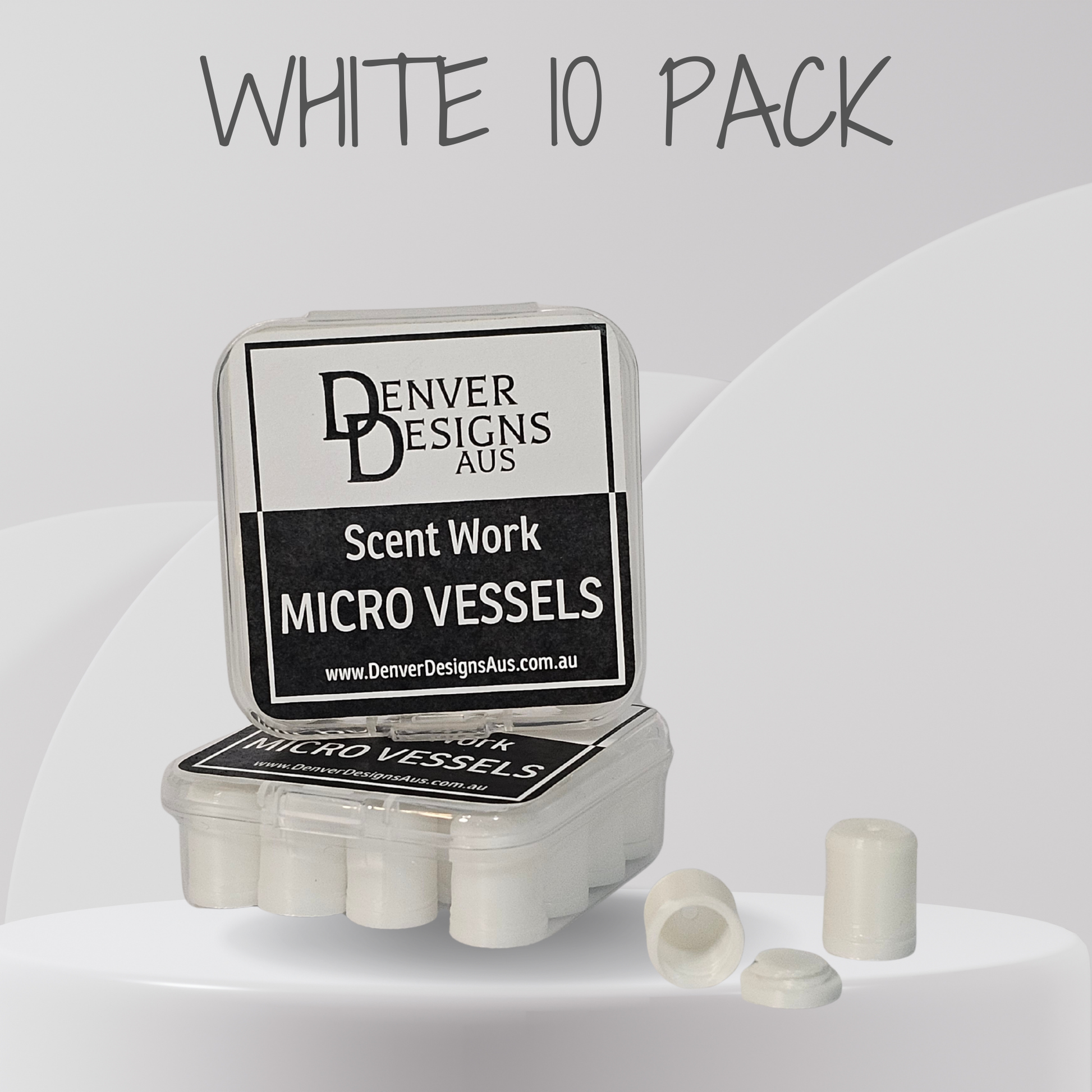 A clear plastic case labeled 'Denver Designs Aus Scent Work Micro Vessels' with a white 'WHITE 10 PACK' text overlay above, showing several small white cylindrical micro vessels and two loose pieces in front on a light gray studio background.