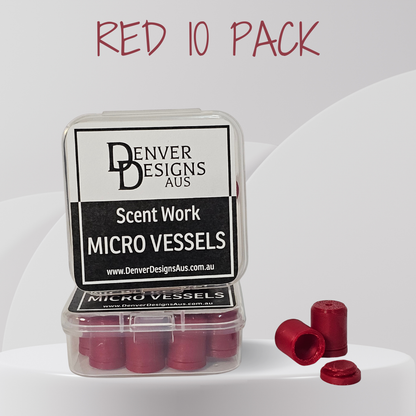 A clear plastic case containing small red cylindrical micro vessels, with three loose red vessels placed beside it on a white studio background. The lid label reads 'Denver Designs Aus' and 'Scent Work Micro Vessels.
