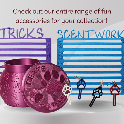 A promotional product shot showing a metallic pink cylindrical treat jar and matching round lid with embossed paw prints and the words 'TREATS FOR TRICKS,' alongside several key-shaped accessories in blue, black, white, and red. Large text reads 'Check out our entire range of fun accessories for your collection!' with 'TRICKS' and 'SCENTWORK' above the items.
