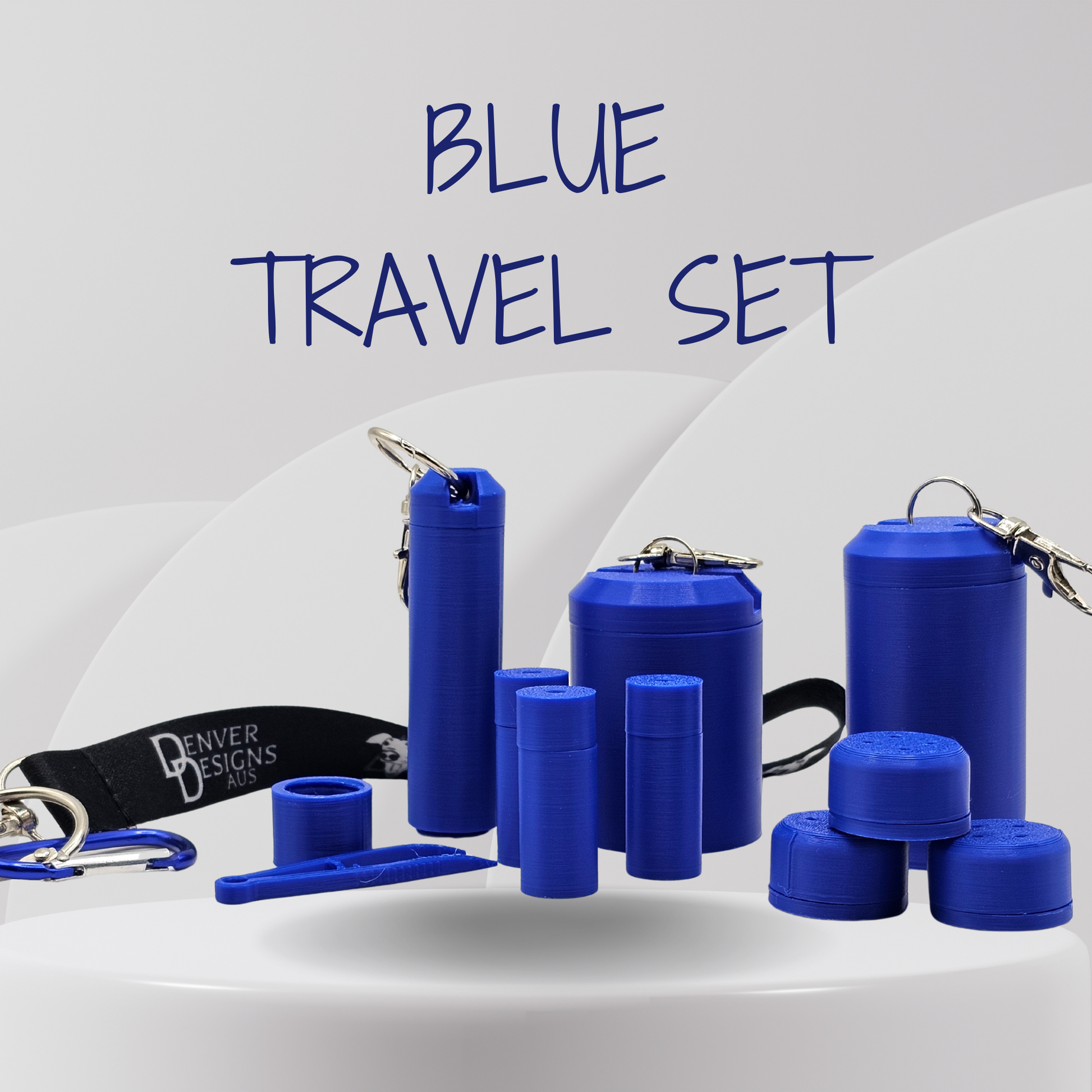 A blue travel set displayed on a white surface against a light gray background, featuring multiple cylindrical containers, small accessories, and a black keychain strap with 'Denver Designs' printed on it. Large text at the top reads 'BLUE TRAVEL SET'.