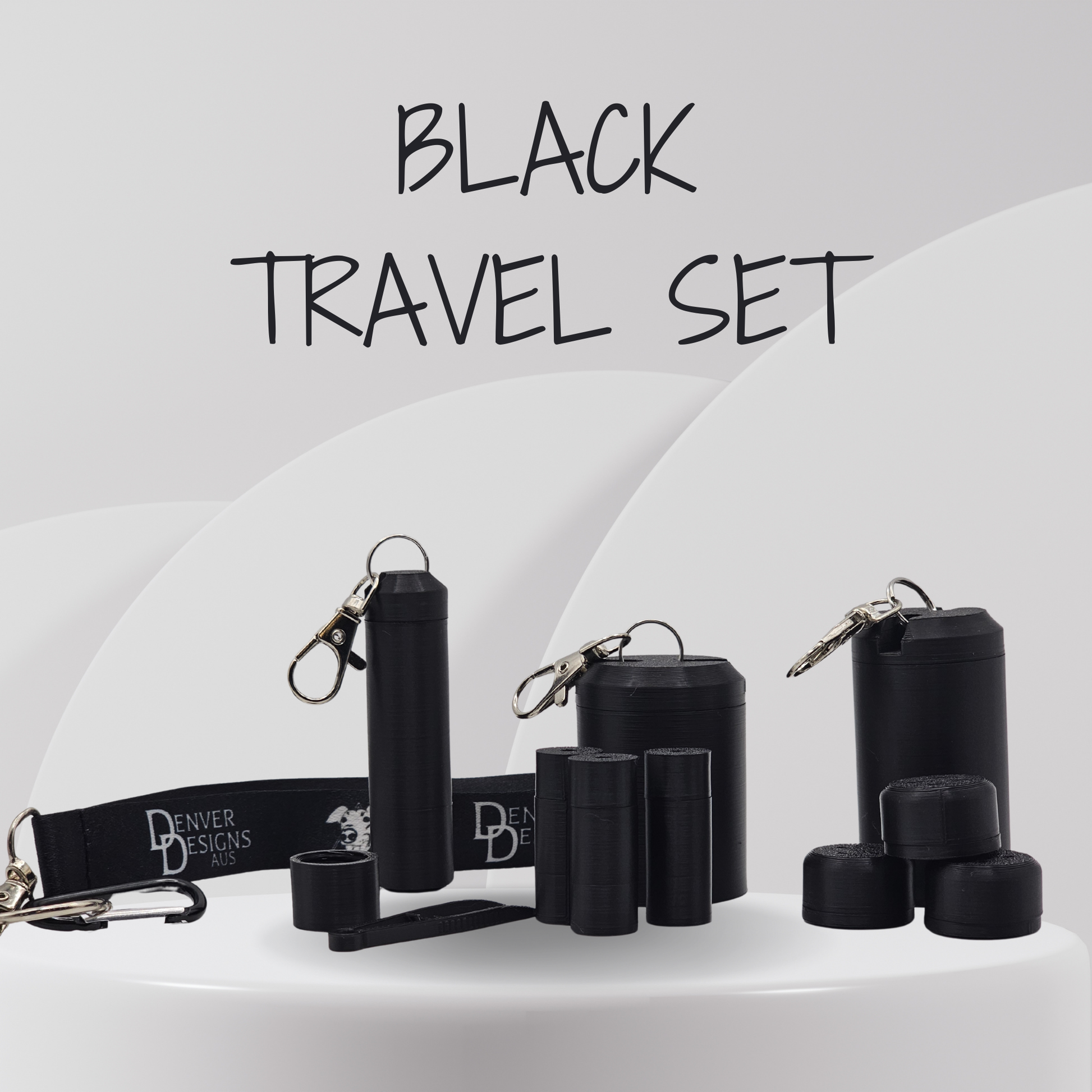 A black travel set displayed on a white pedestal, including cylindrical containers, small caps, a wrist strap with 'Denver Designs' branding, and metal keychains, with the text 'BLACK TRAVEL SET' above.