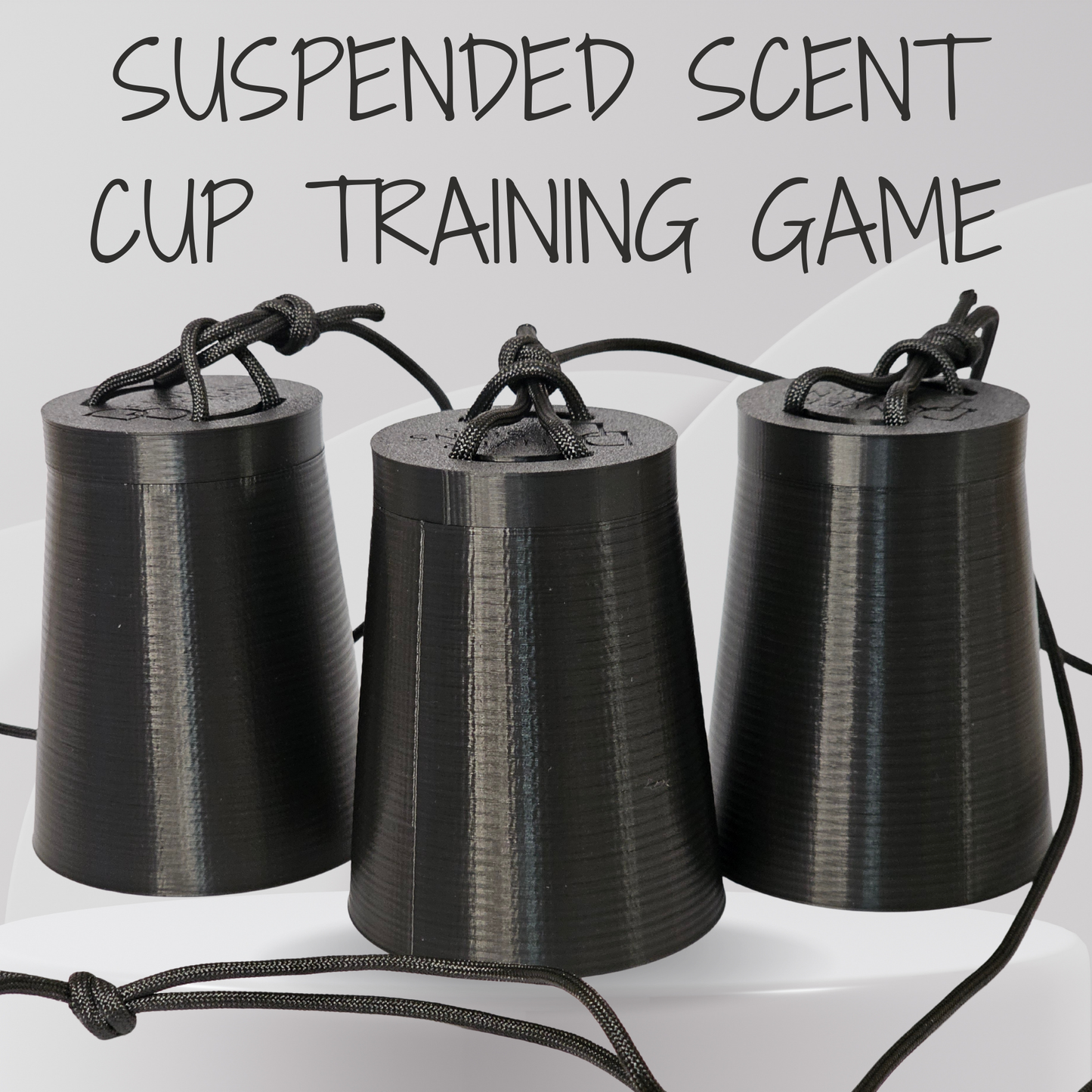 Three black 3D-printed cone-shaped cups hanging from black cords, with the text 'SUSPENDED SCENT CUP TRAINING GAME' above them on a light gray background.