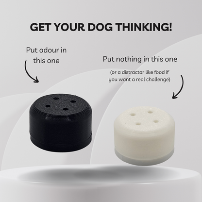 Two cylindrical dog training scent vessels shown on a light gray background with explanatory text. The left vessel is black and labeled 'Put odour in this one,' and the right vessel is white and labeled 'Put nothing in this one (or a distractor like food if you want a real challenge).